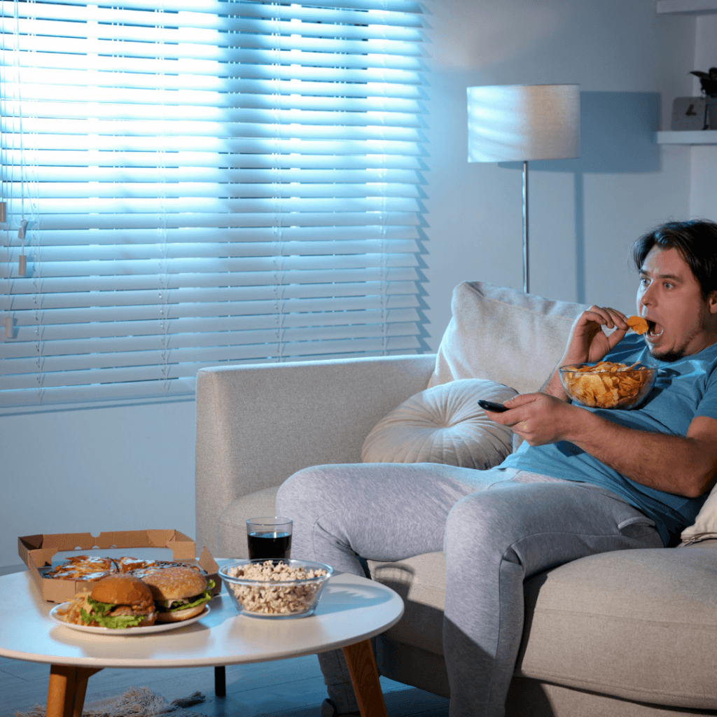 Mann sitzt auf dem Sofa und stopft ungesundes Essen in sich hinein