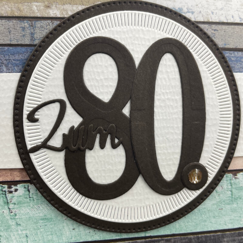 Detail der Banderole: großer Kreis in Espresso mit Strahlenmuster in Grundweiß und dem Schriftzug zum 80.