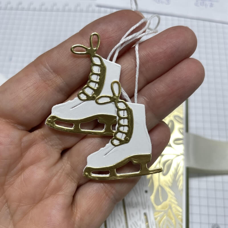 Zwei gestanzte Schlittschuhe in Grundweiß und Gold, leicht versetzt übereinandergeklebt, liegen auf der Hand