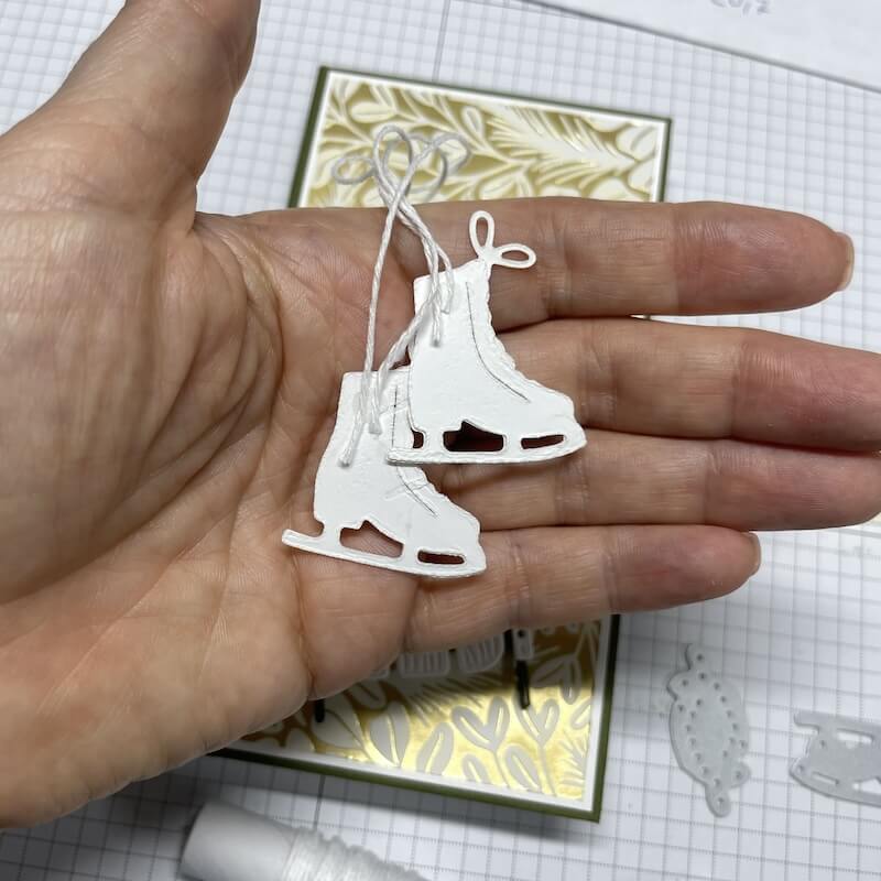 Rückseite der Schlittschuhe mit angeklebtem Bändchen, dahinter die Schachtel mit grün-goldenem Designerpapier