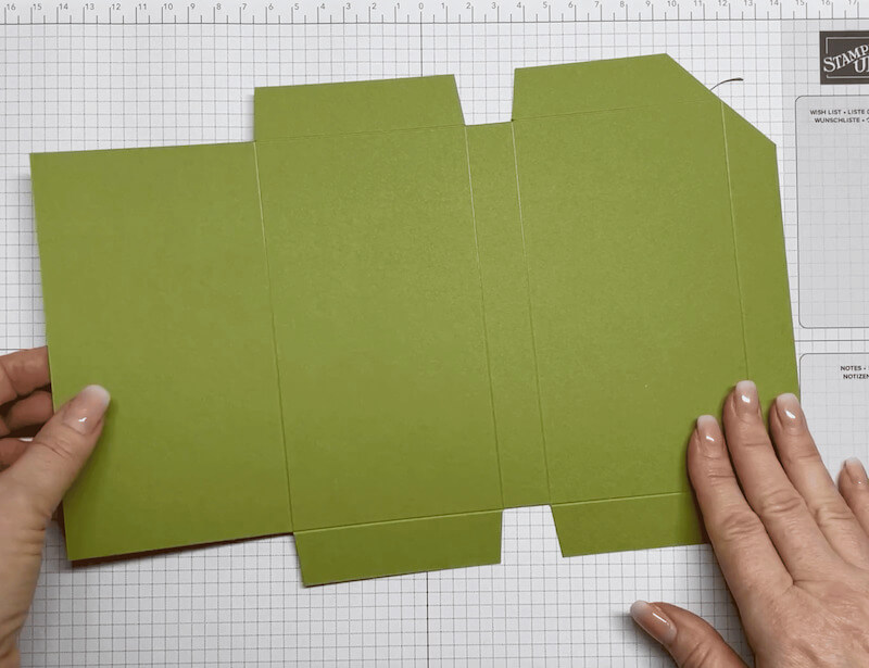 Zugeschnittener Umschlag aus Waldmoos-Karton flach ausgelegt, mit schmalen Klebefalzen und Einschnitten für den Buchrücken