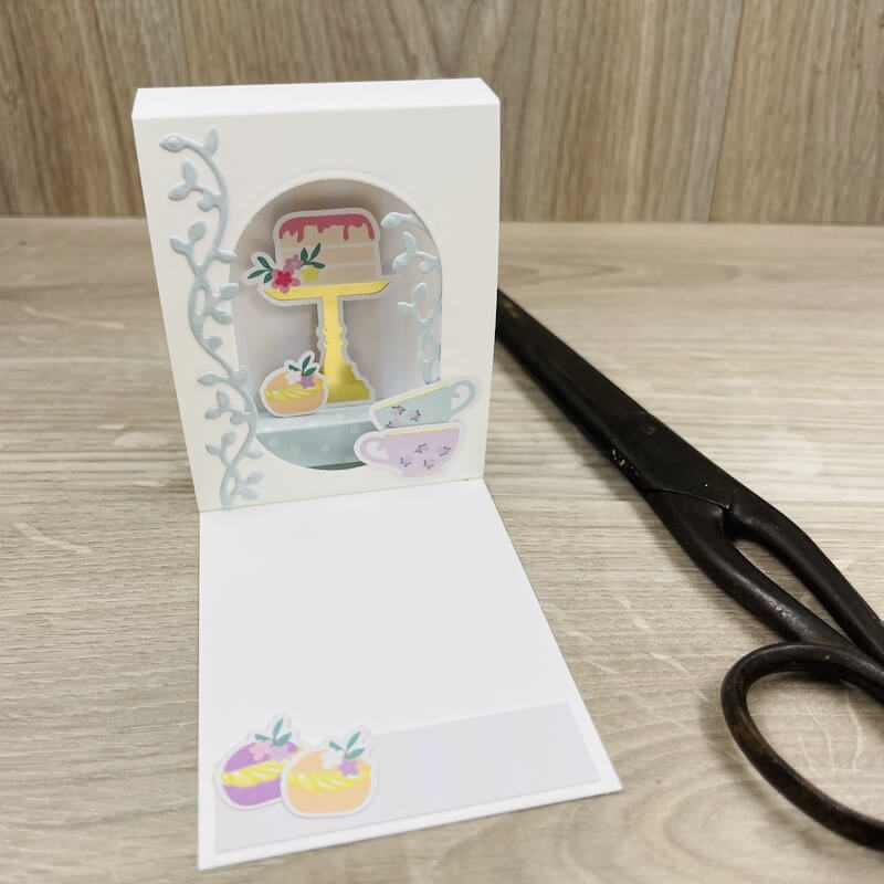 Karte 11 als Mini-Aufstellkarte in Weiß mit Bogenfenster, blauen Ranken und Torte auf einer Etagere