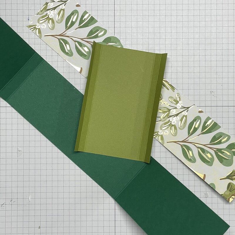Grüne Kartonhülle und floral-goldener Designerpapierstreifen auf der Schneidematte