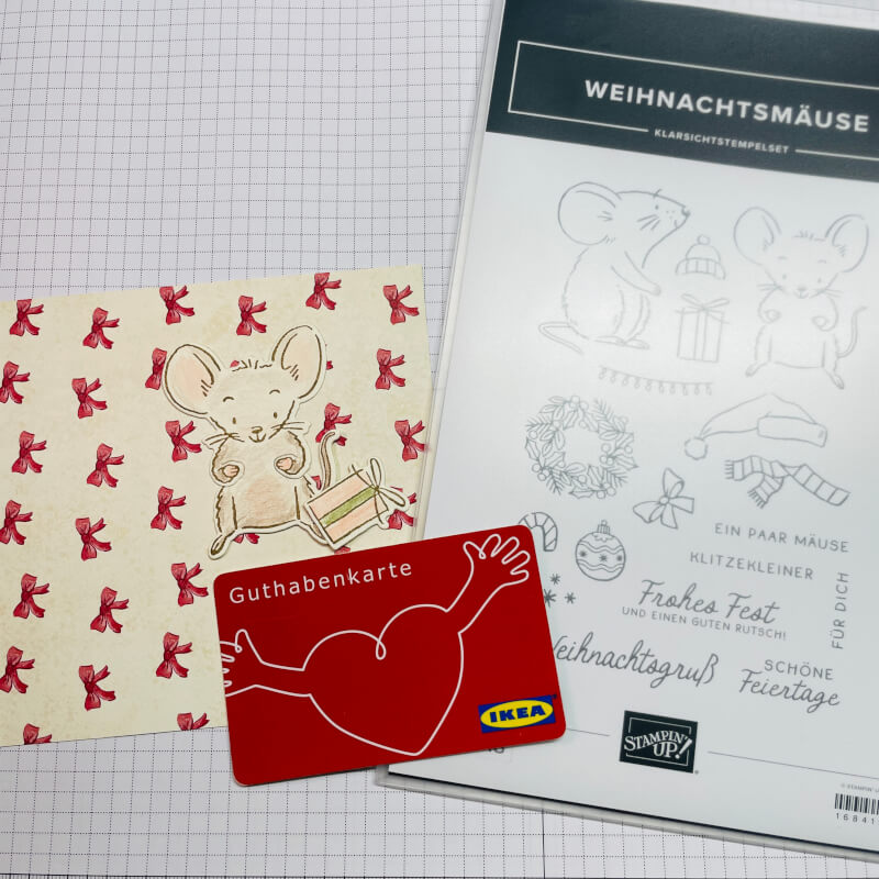 Material zum Kleinigkeiten verpacken: Stempelset Weihnachtsmäuse, Designerpapier mit roten Schleifen, eine gestempelte Maus und eine Gutscheinkarte auf der Schneidematte