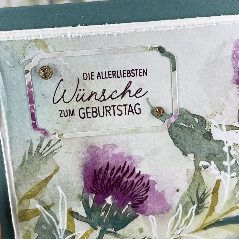 Detail der Vintage-Karte mit angerautem Rand, Distelmuster und Etikettrahmen um den Gruß in Brombeermousse