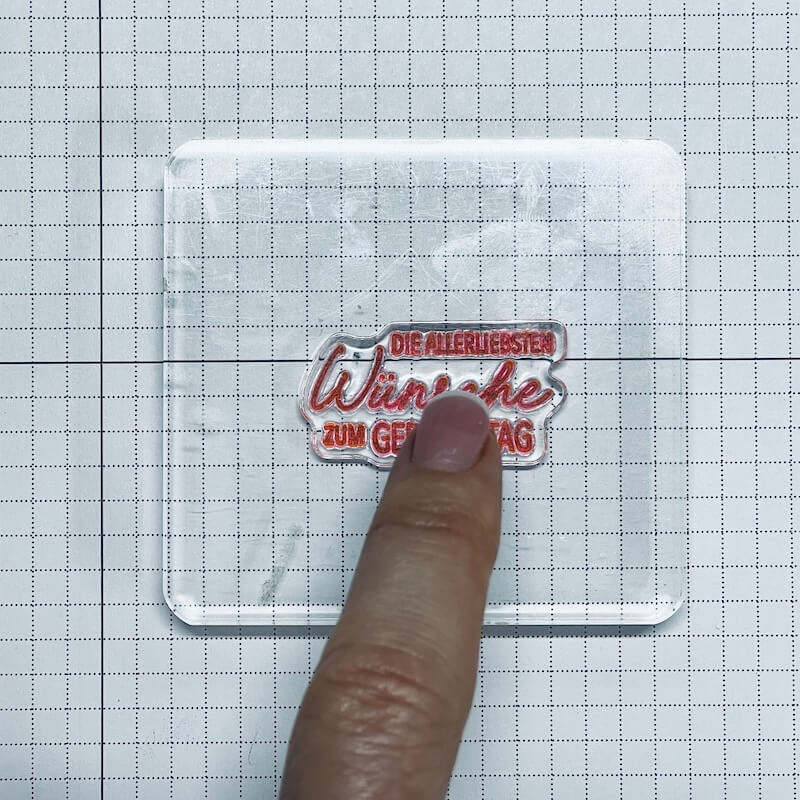 Finger drückt einen Klarsichtstempel mit Geburtstagsgruß auf eine Stempelplatte