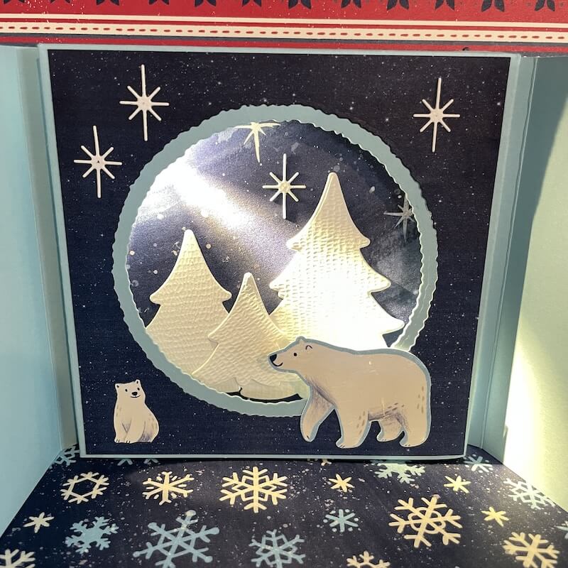 Karte in Weiß und Blau mit gestanzten Sternen, Tannen und zwei Eisbären