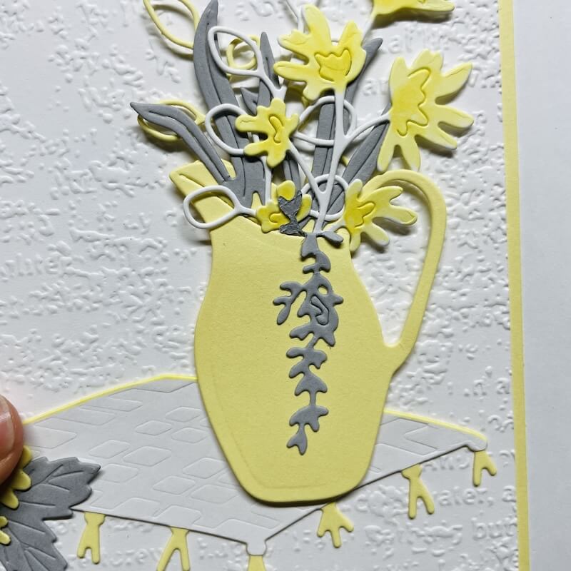 Bastelbeispiel mit Zeitlose Zierde: gelber Krug als Vase mit gestanzten Blüten und Blättern auf geprägtem Weiß