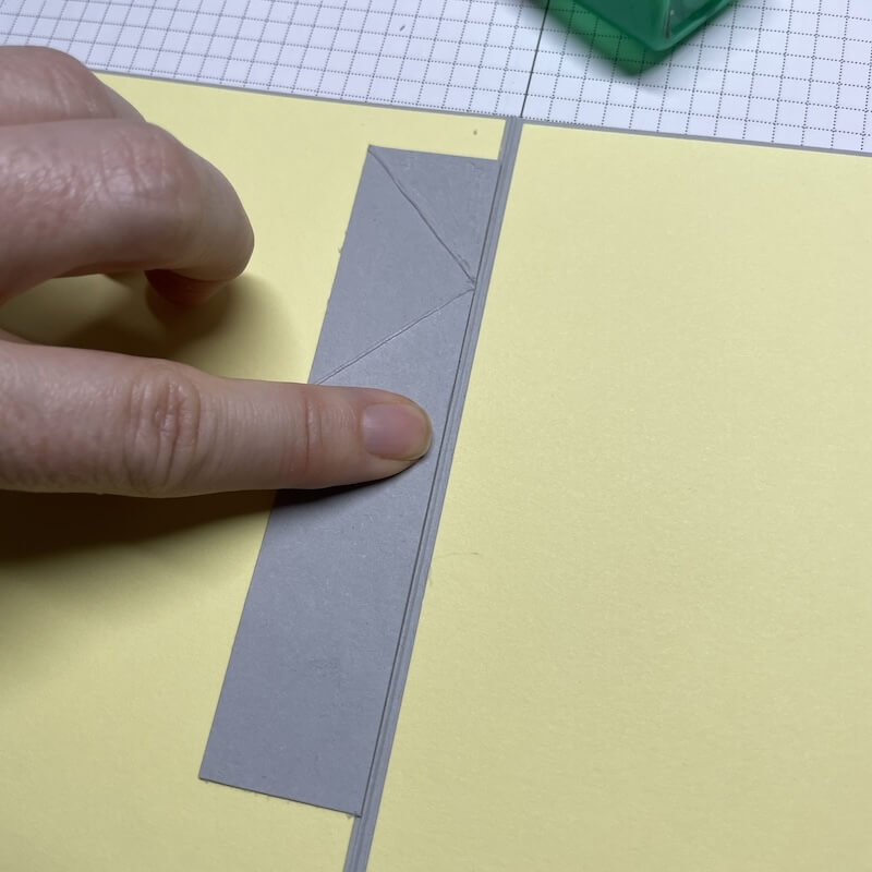 Der angeklebte Streifen zeigt nach unten und liegt parallel zur Kartenmitte, ein Finger drückt ihn an