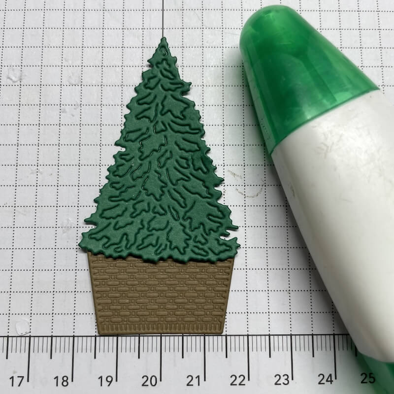 Ausgestanzter grüner Tannenbaum mit Korb-Unterteil neben dem Klebestift