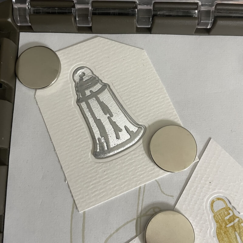 Silbern geprägte Glocke und drei Magnete auf dem Kartonzuschnitt