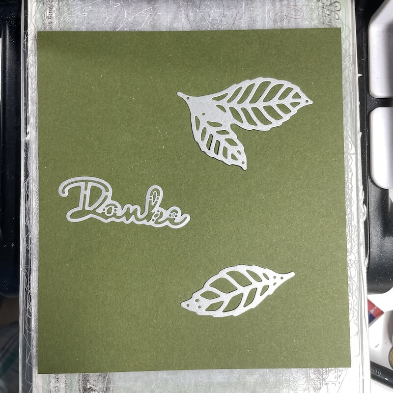 Farbkarton in Waldmoos mit ausgestanzten Blättern und dem Schriftzug Danke