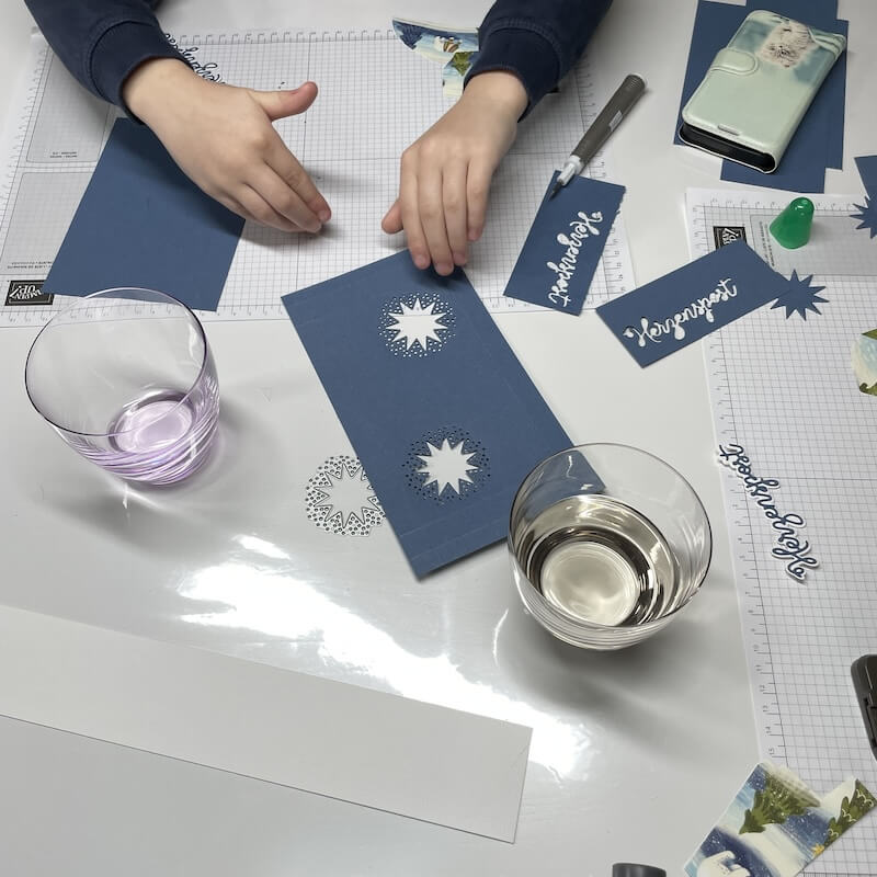 Kinderhände arbeiten im Workshop an den blauen Verpackungen und Etiketten auf der Schneidematte