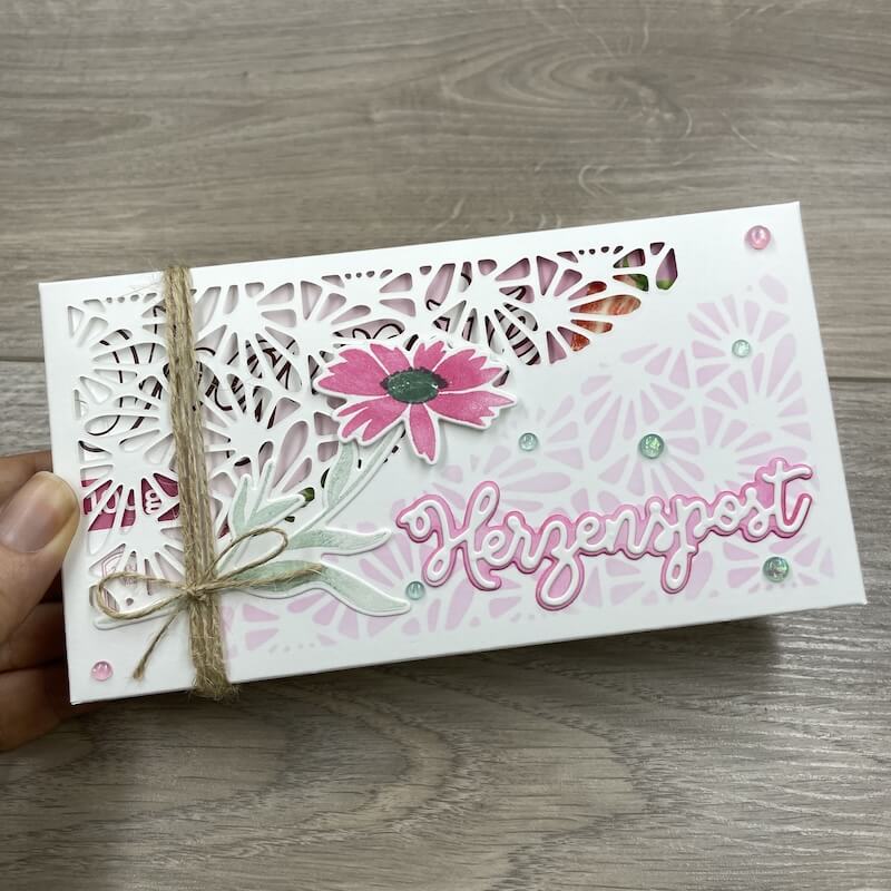 Hand hält die weiß-rosa Blumenverpackung mit Juteband und Schriftzug Herzenspost