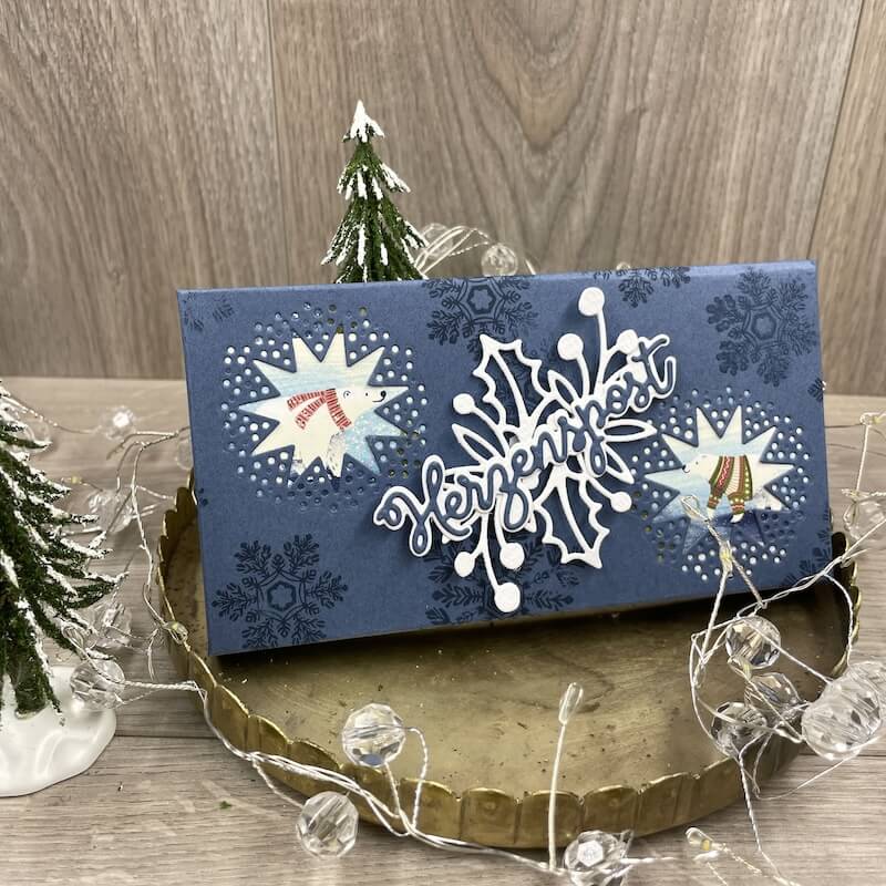Dunkelblaue Schokoladenverpackung mit Schneeflocken, Eisbär und Schriftzug Herzenspost auf Goldteller