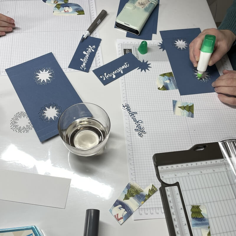 Hand trägt mit dem grünen Klebestift Kleber auf die blauen Projektteile auf