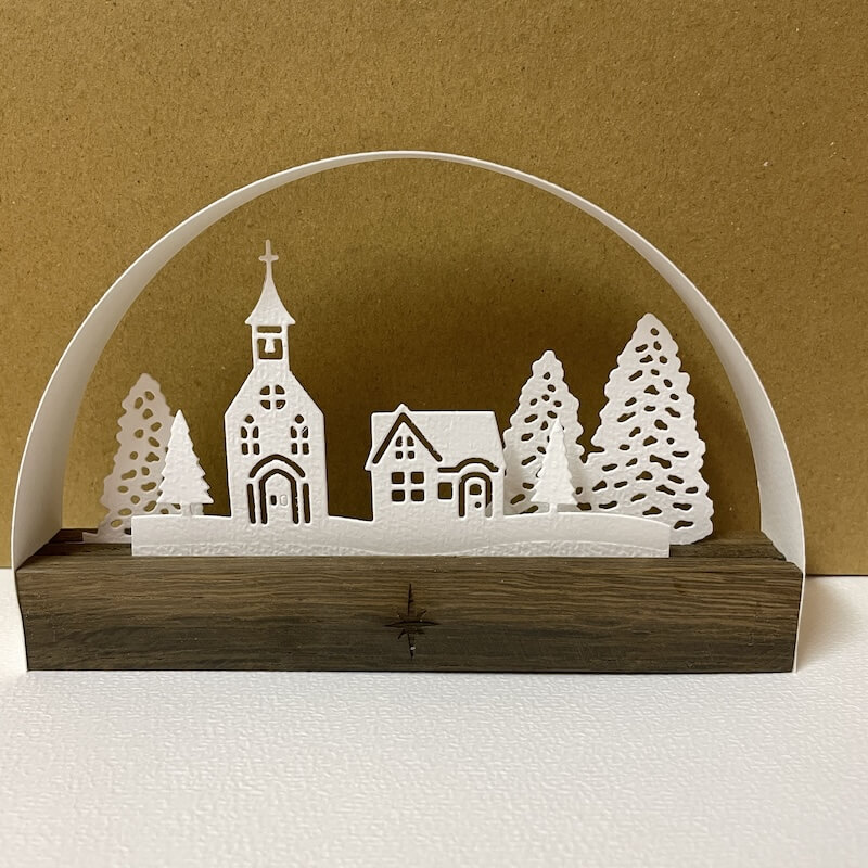 Kirche mit Wohnhaus und Tannen auf einem dunklen Holzsockel mit Stern