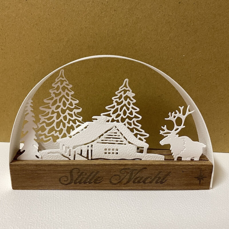 Hütte mit Rentier und filigranen Tannen, dunkler Sockel mit Stille Nacht