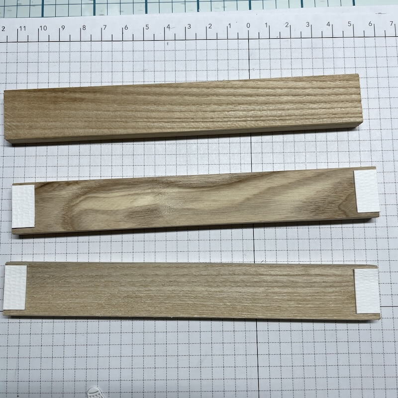 Drei Holzleisten, zwei davon mit schmalen Papierstreifen als Abstandshalter beklebt