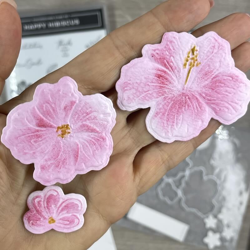 Zwei rosa kolorierte Hibiskusblüten mit geprägter Struktur in der Hand