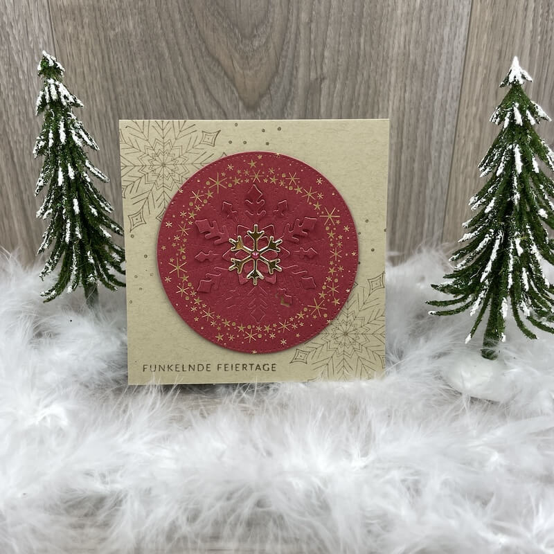 Goldene Karte mit rotem Kreis und Schneeflocke zwischen Deko-Tannen
