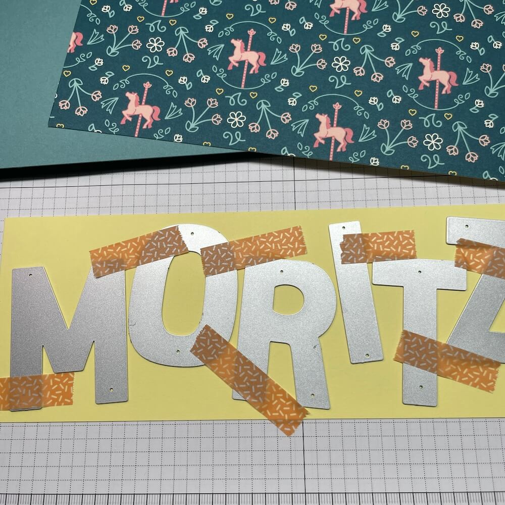 Mit Washitape befestigte Buchstabenstanzen auf dem gelben Aufleger, bereit für die Stanz- und Prägemaschine