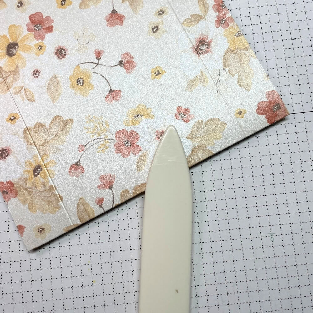 Papierfalter streicht die Falzlinien im geblümten Designerpapier für den Deckel nach