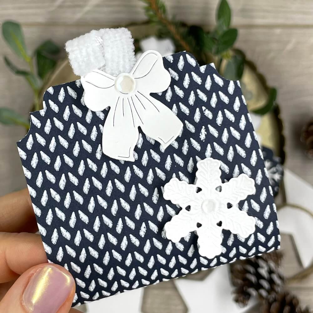 Weihnachtliches Goodie aus dunkelblauem Papier mit erhabenem Muster, weißer Schleife und Schneeflocke