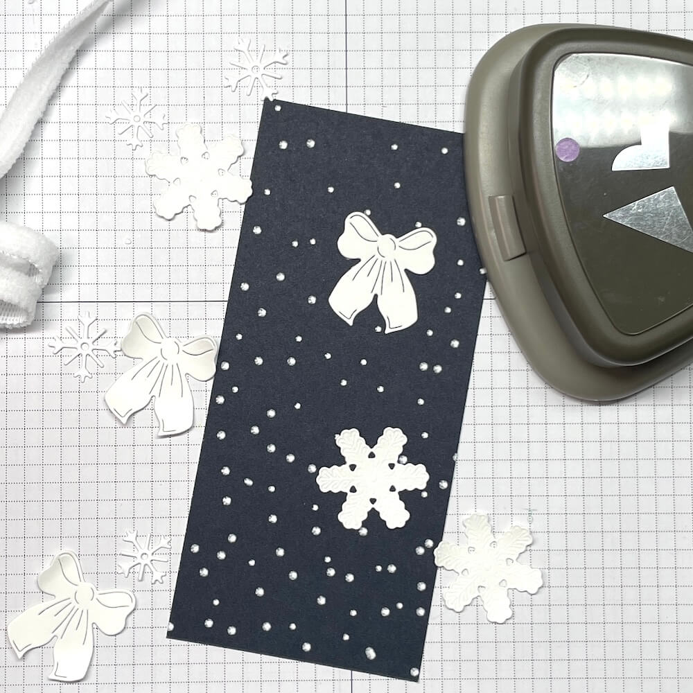 Zugeschnittener Streifen Designerpapier neben der Stanze und gestanzten Schneeflocken