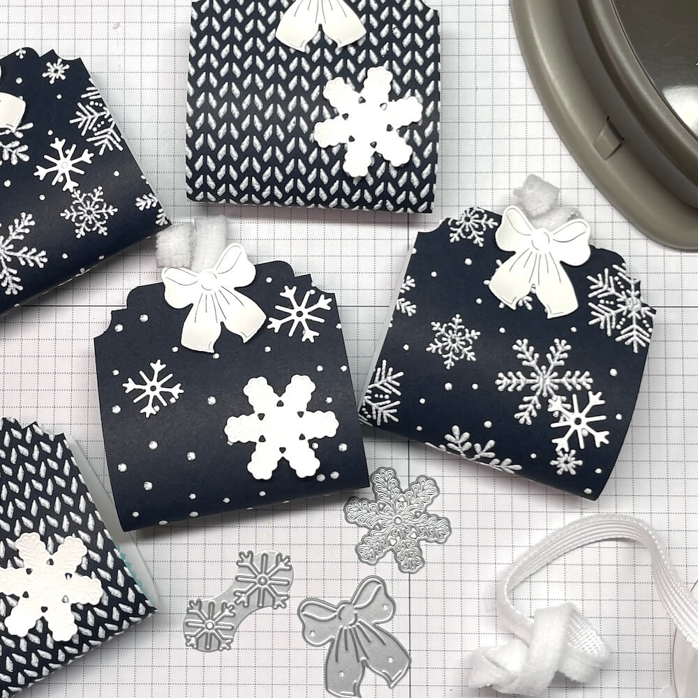 Fertige Weihnachts-Goodies mit Schneeflocken-Stanzformen und weißem Schleifenband auf der Schneidematte