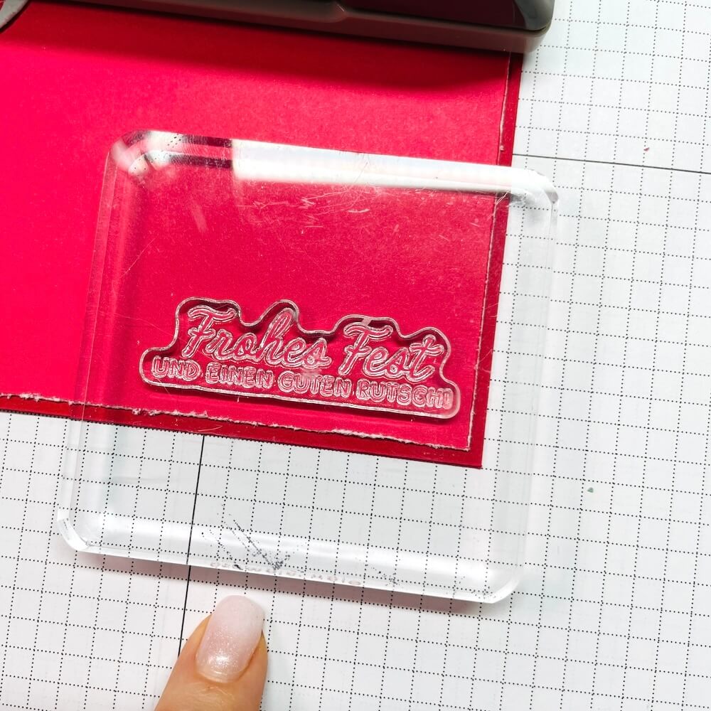 Der Spruch Frohes Fest und einen guten Rutsch liegt auf dem Acrylblock über dem glutroten Karton