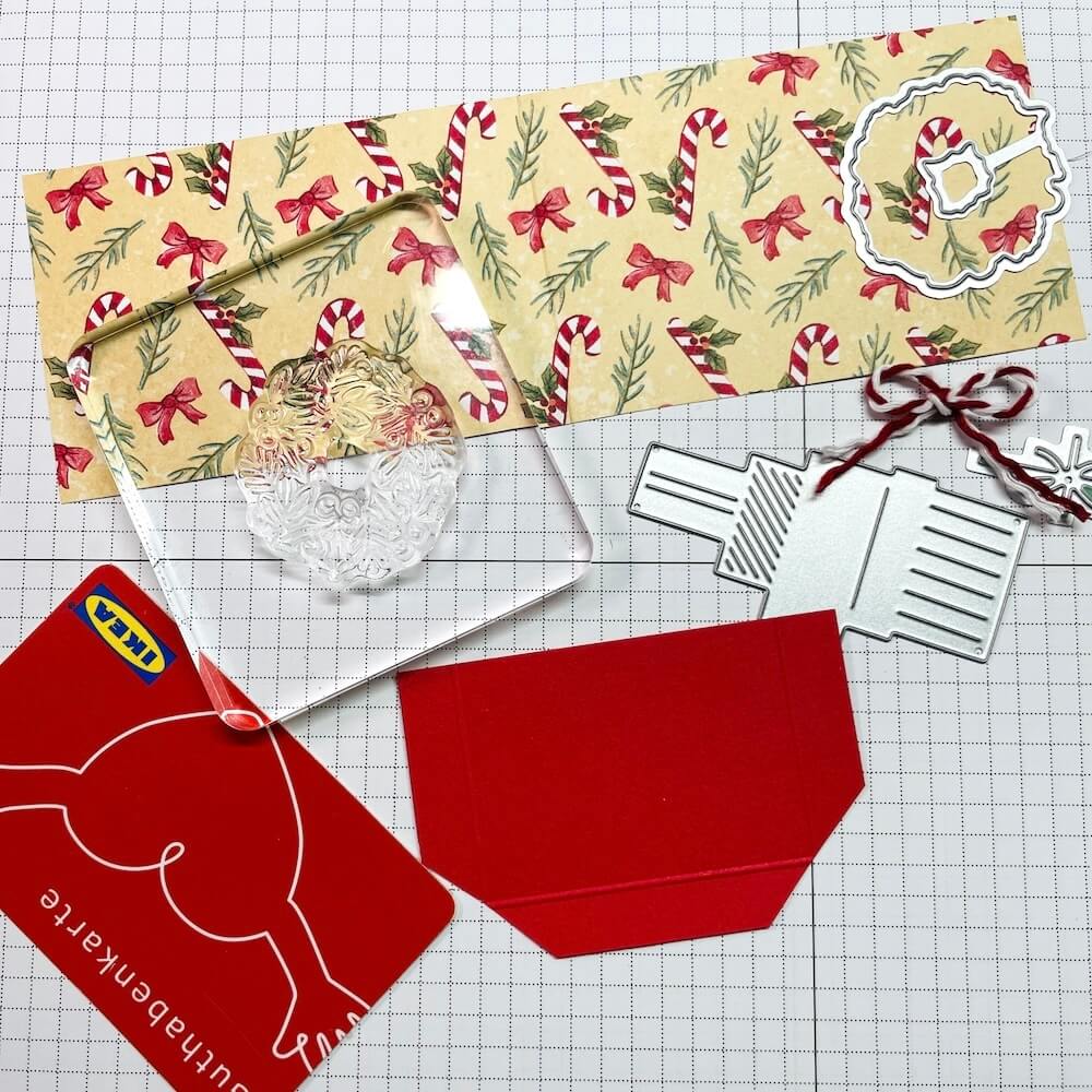 Zugeschnittenes Designerpapier, Stanzformen für Geschenkestapel und Kranz, glutroter Karton und die Gutscheinkarte