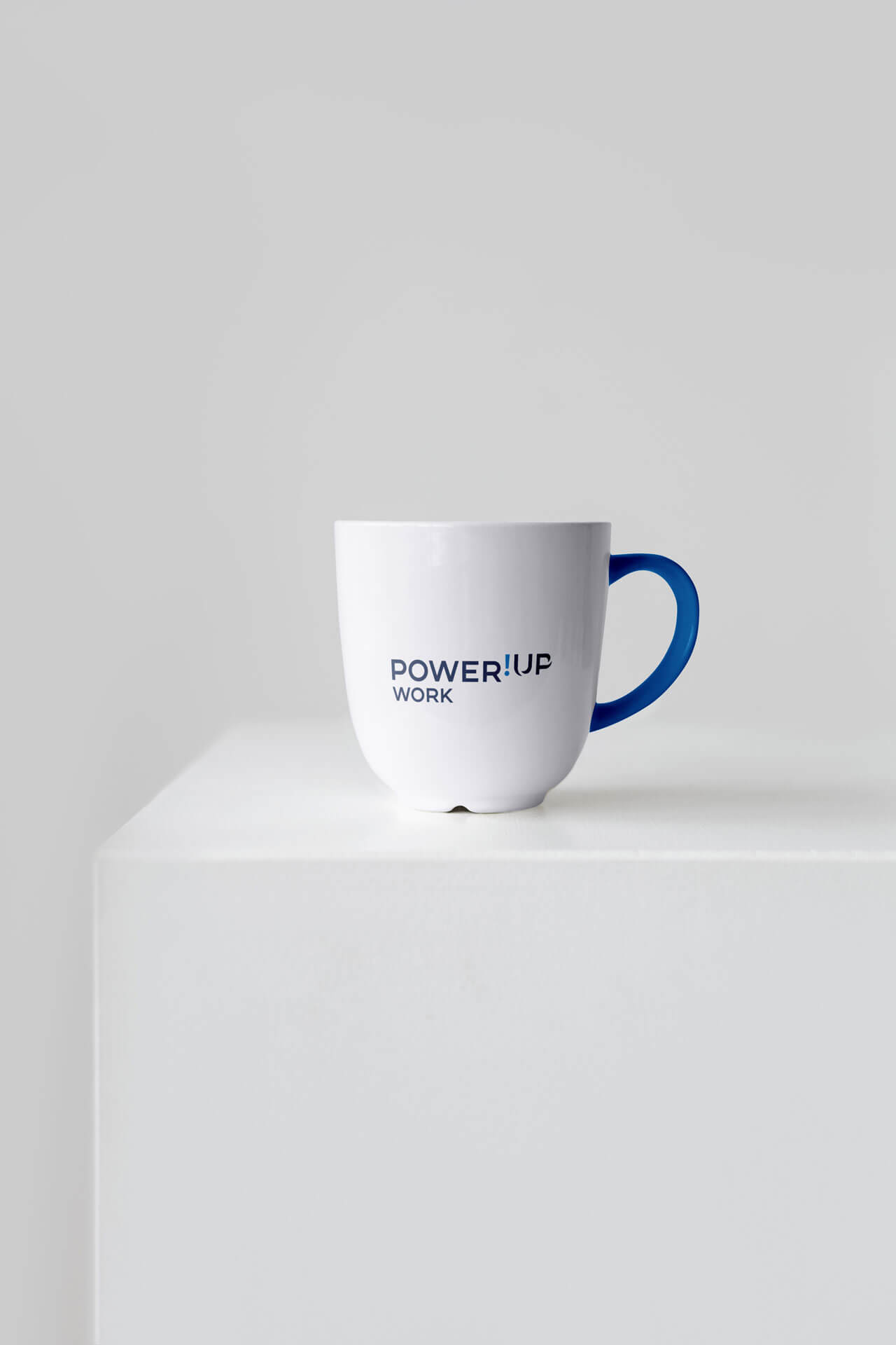 Power!Up-Work-Logo auf minimalistischer weißer Tasse mit blauem Henkel und hellem Hintergrund