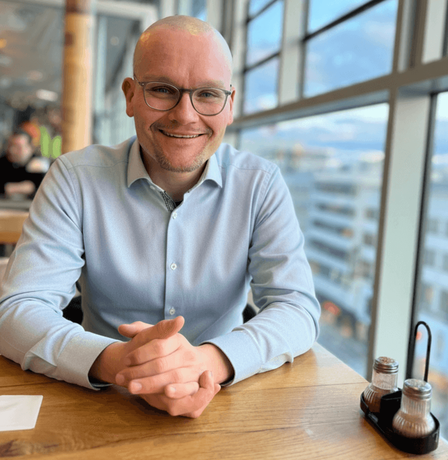 Oliver Haas sitzt in einem hellblauen Hemd an einem Tisch und lächelt in die Kamera