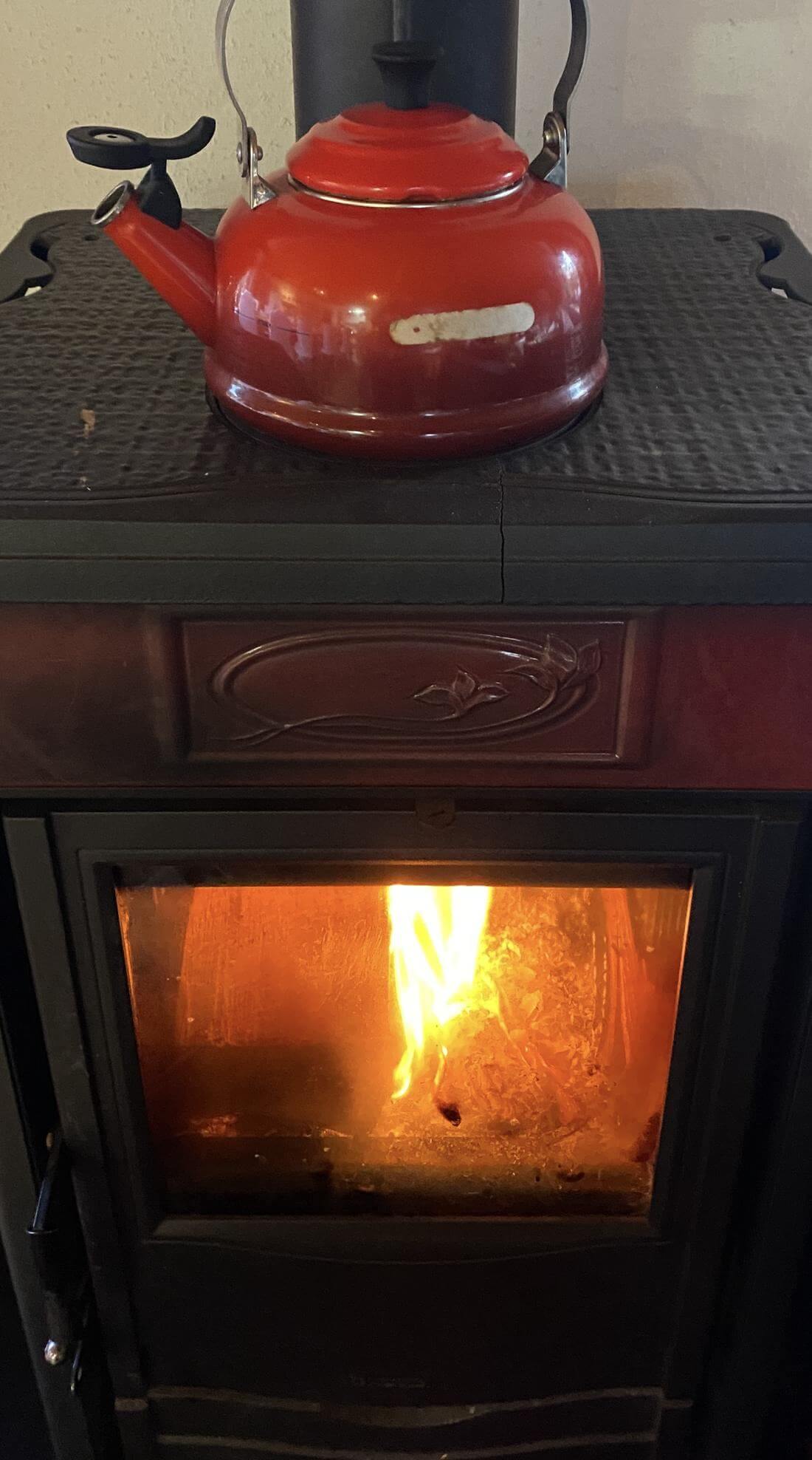 Holzofen mit brennendem Feuer, darauf ein roter Wasserkessel