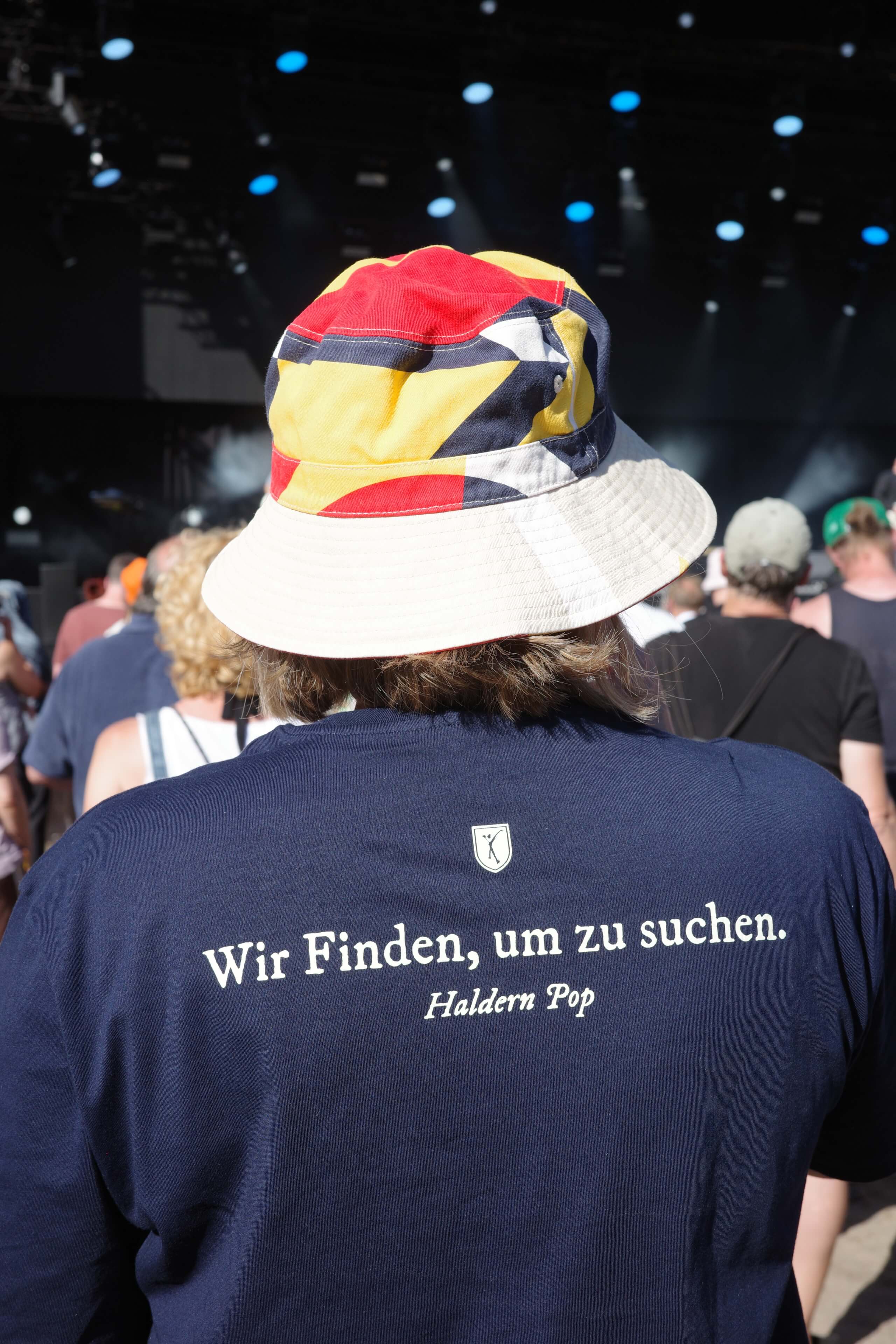 Melanie steht mit ihrem Haldern Pop-Shirt vor der Bühne; auf ihrem Rücken steht „Wir finden, um zu suchen."