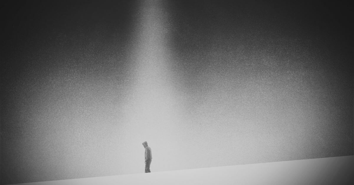 Symbolbild für Einsamkeit: eine alleinstehende Person mit Kapuze im grauen Lichtkegel – Ausdruck von Isolation und innerer Leere.