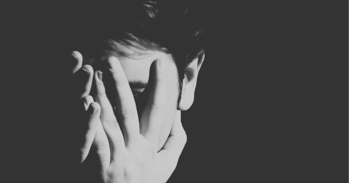 Schwarz-Weiß-Foto einer Person, die ihr Gesicht mit der Hand verdeckt – Symbol für Scham, Rückzug und innere Belastung.