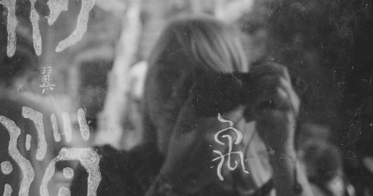 Schwarz-weiß-Foto einer Person, deren Spiegelbild verschwommen zu sehen ist – symbolisch für Identität, Selbstbild und gesellschaftlichen Druck zur Selbstoptimierung.