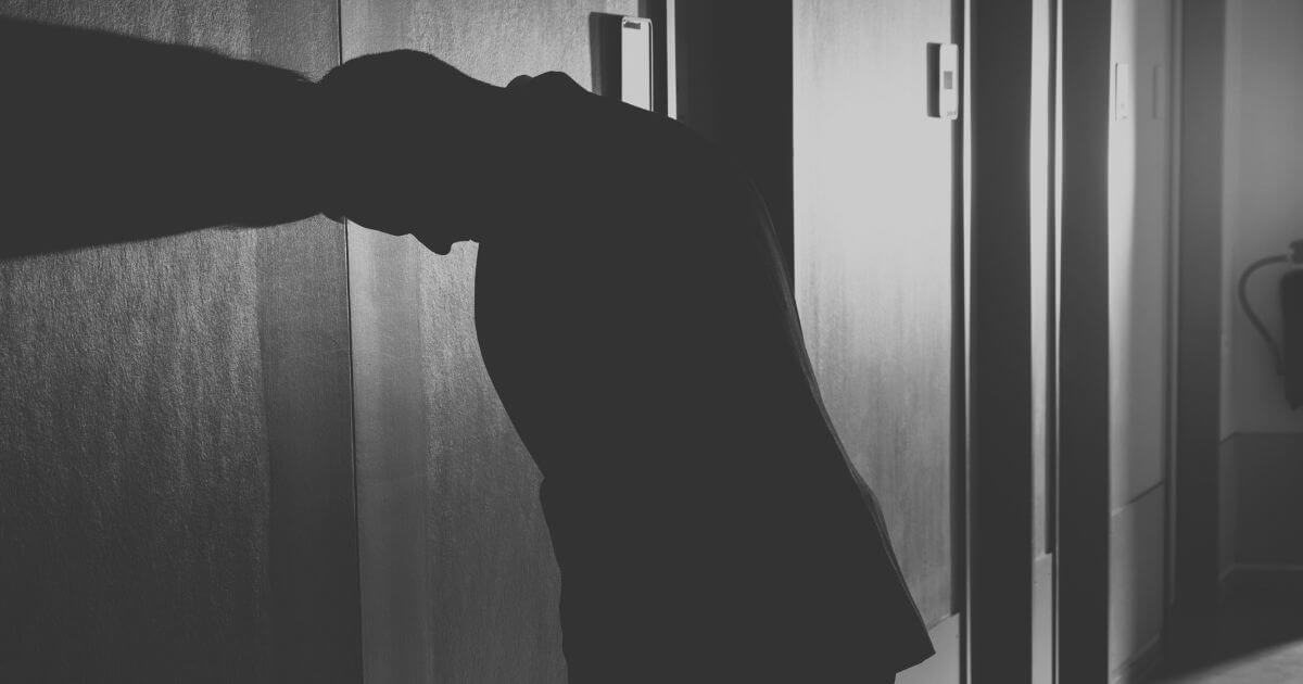 Silhouette einer erschöpften Person, die sich mit dem Kopf an eine Wand lehnt – Symbol für Überforderung, Selbstkritik und die Angst vor Fehlern.