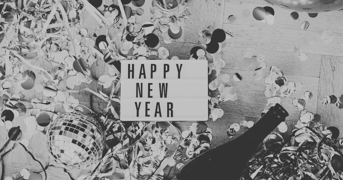 Schwarz-weißes Stillleben zum Jahreswechsel mit Konfetti, Sektflasche und Leuchtschild ‚Happy New Year‘ – Symbol für Übergang statt Neubeginn.