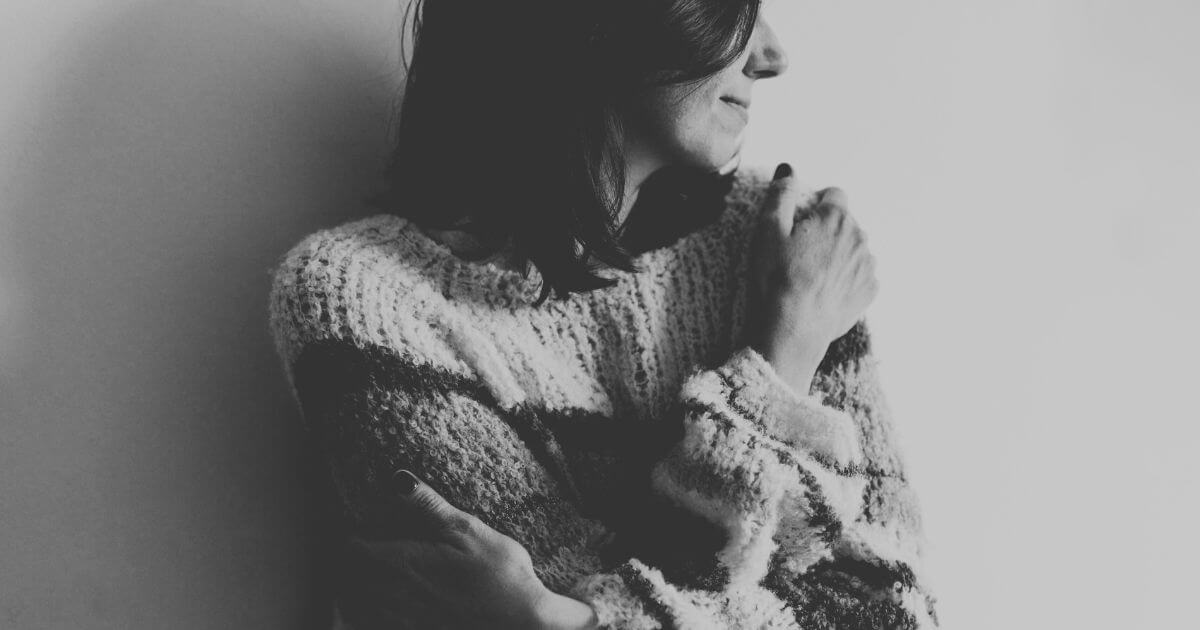 Frau hält sich selbst in einem stillen Moment – Symbol für Selbstmitgefühl im Umgang mit innerer Belastung.