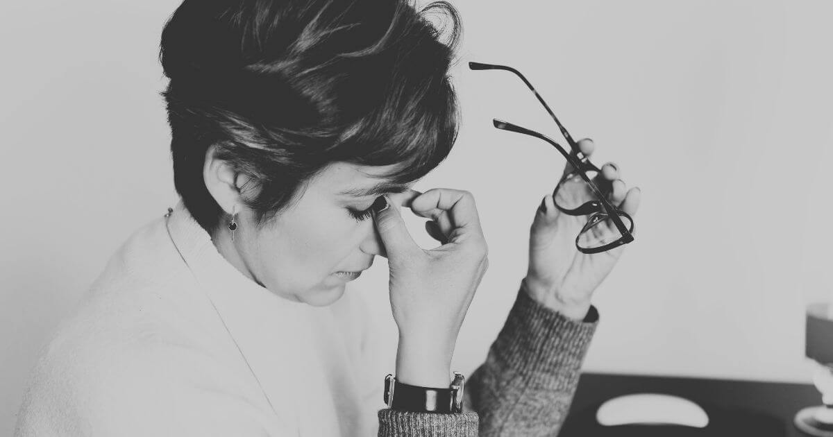 Frau sitzt nachdenklich mit geschlossenen Augen und hält ihre Brille in der Hand – Symbolbild für Überanpassung im Erwachsenenalter und emotionale Erschöpfung