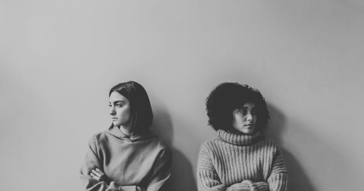 Zwei Frauen sitzen nebeneinander und schauen in entgegengesetzte Richtungen – Sinnbild für Kommunikation und Missverständnisse in Beziehungen