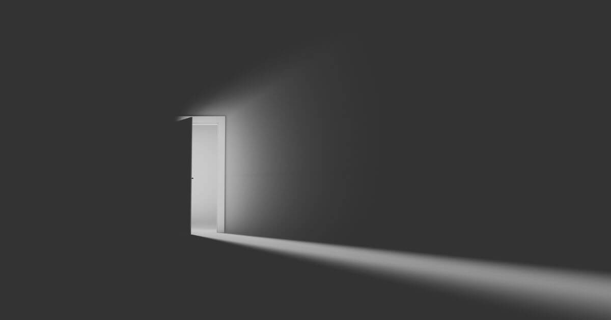 Halb geöffnete Tür mit Lichtstrahl in dunklem Raum als Symbol für Veränderung, Loslassen und den Schritt aus Vertrautem ins Ungewisse.