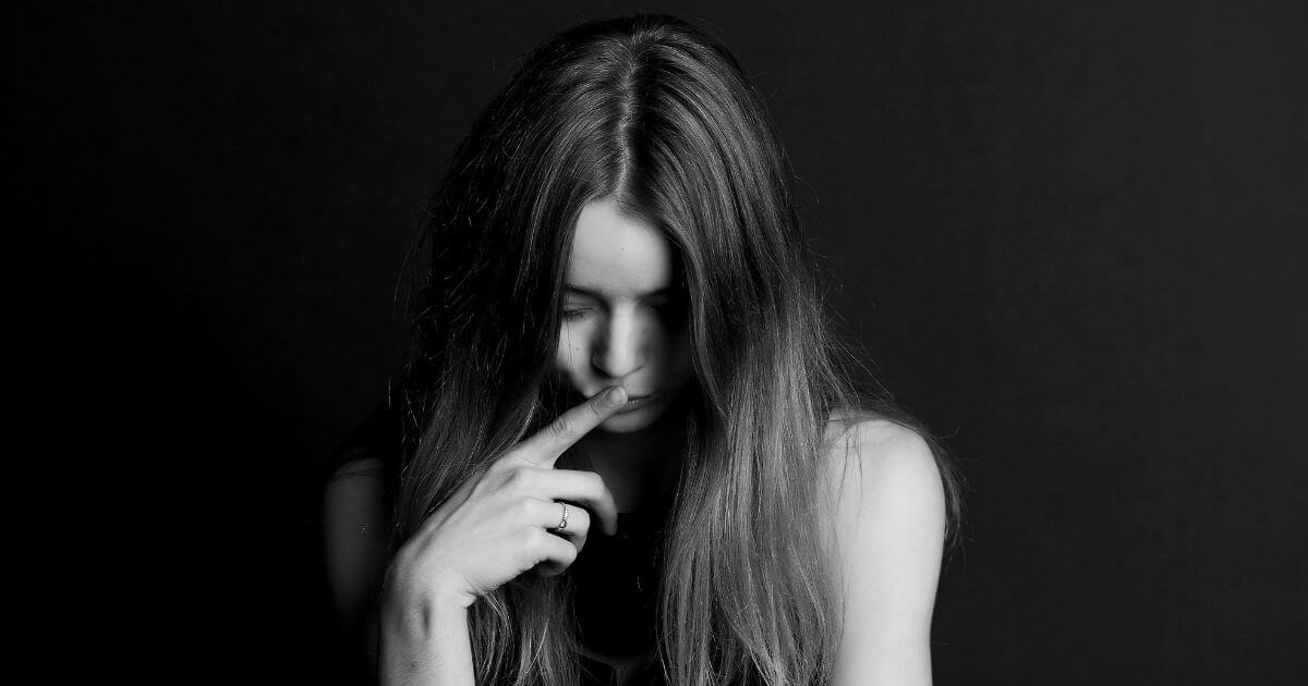 Nachdenkliche Person blickt nach unten mit Hand am Gesicht – symbolisches Bild für Scham, innere Verletzlichkeit und emotionale Prozesse.